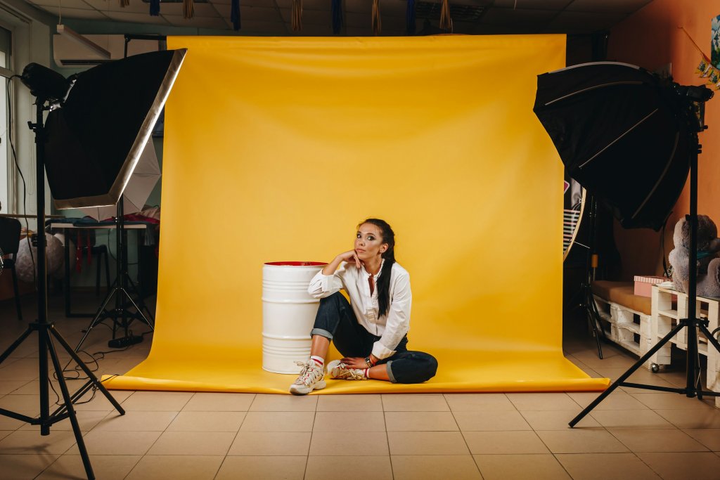 Creative photo studio with yellow backdrop, professional lighting setup, and a model sitting on the floor during a photoshoot